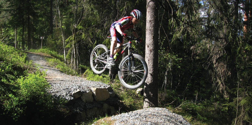 En syklist i full fart over et hopp i skogen