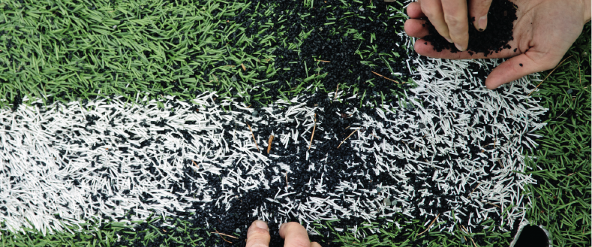 Nærbilde av fire hender som samler gummigranulat på kunstgressbane