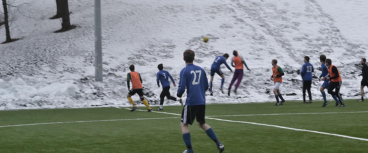 To lag spiller fotballkamp på kunstgressbane på vinterstid