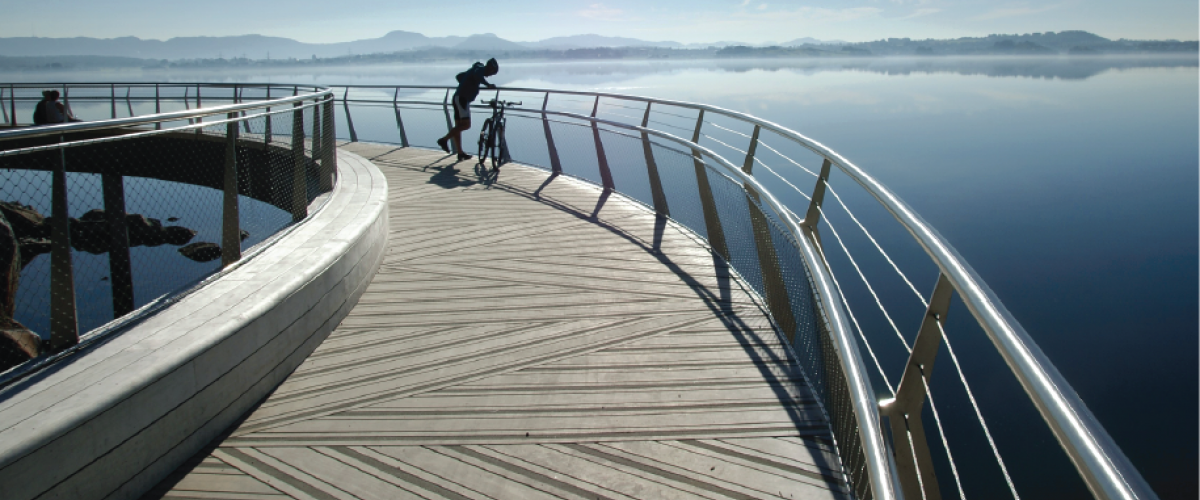 Syklist på bro med utsikt over fjorden.