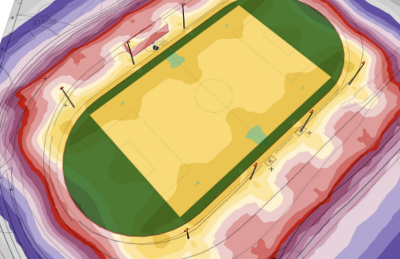 Lysberegningsskisse for Bruvollen stadion sett ovenfra, med kunstgressbanen i midten, løpebanen rundt og åtte markerte lysmaster, omgitt av fargelagte soner som viser lysstyrke og spredning.